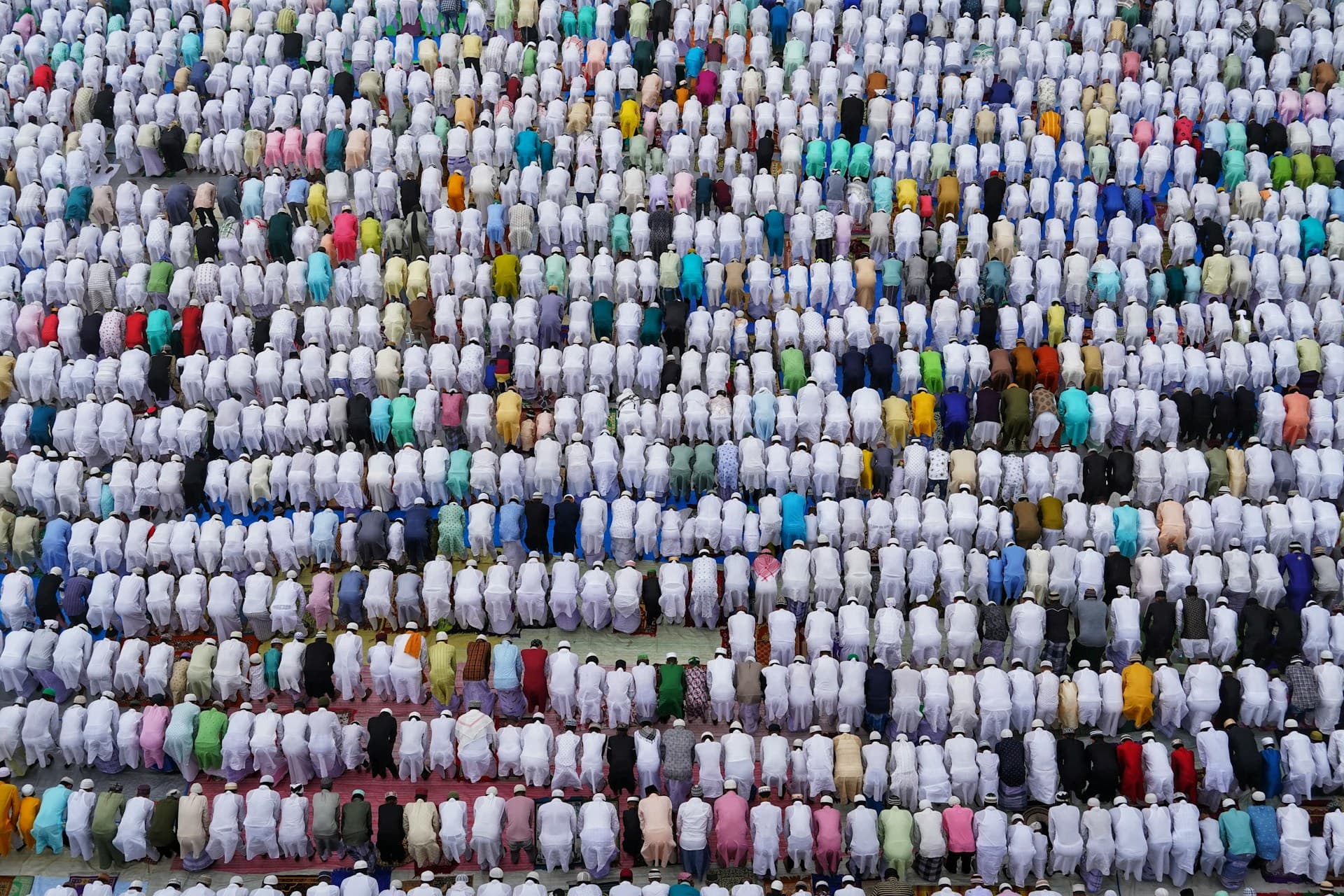 A bird's eye view shows a large group of Muslims kneeling down in prayer together