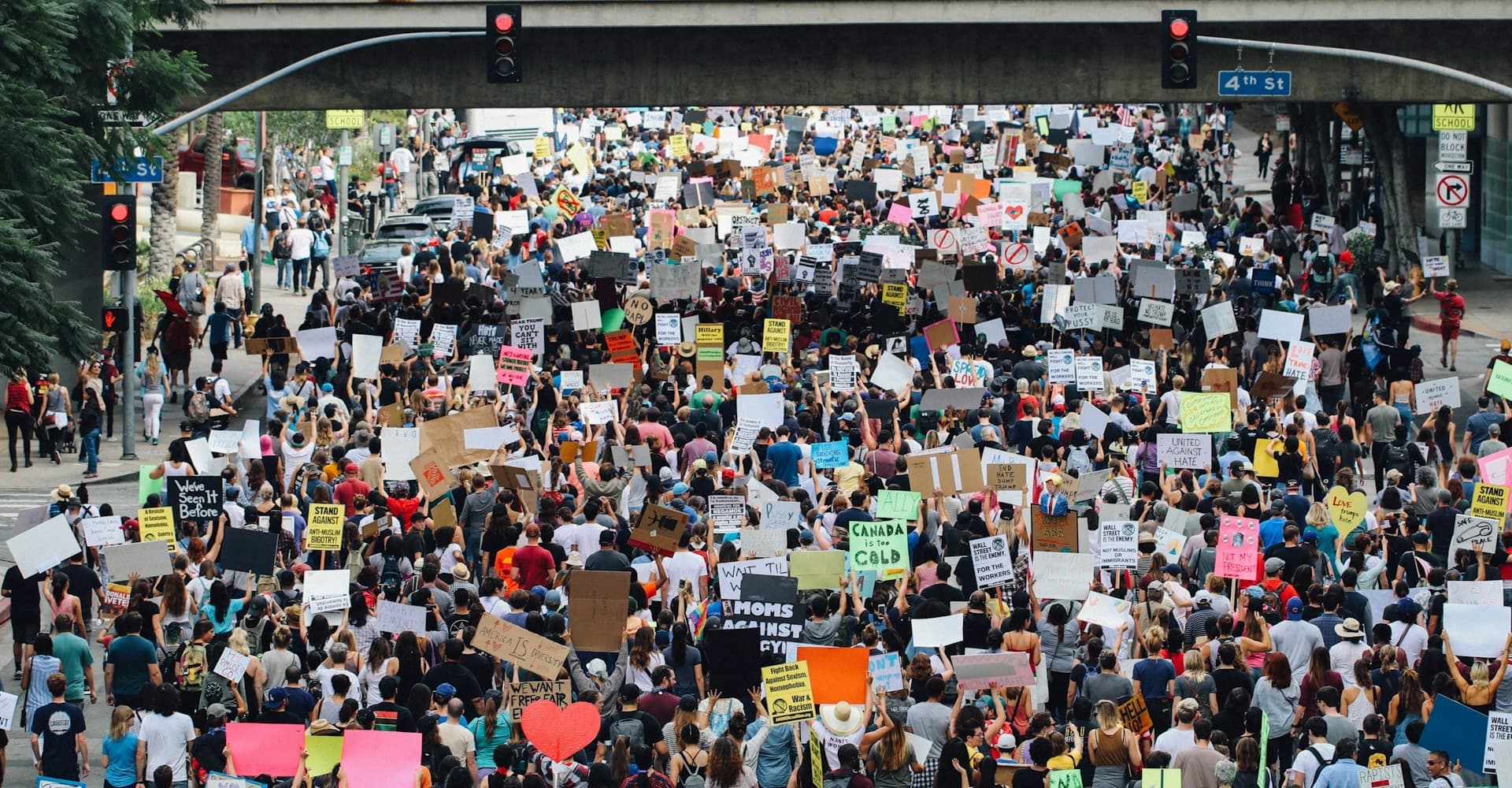 A large group of people stand in the street holding signs in protest