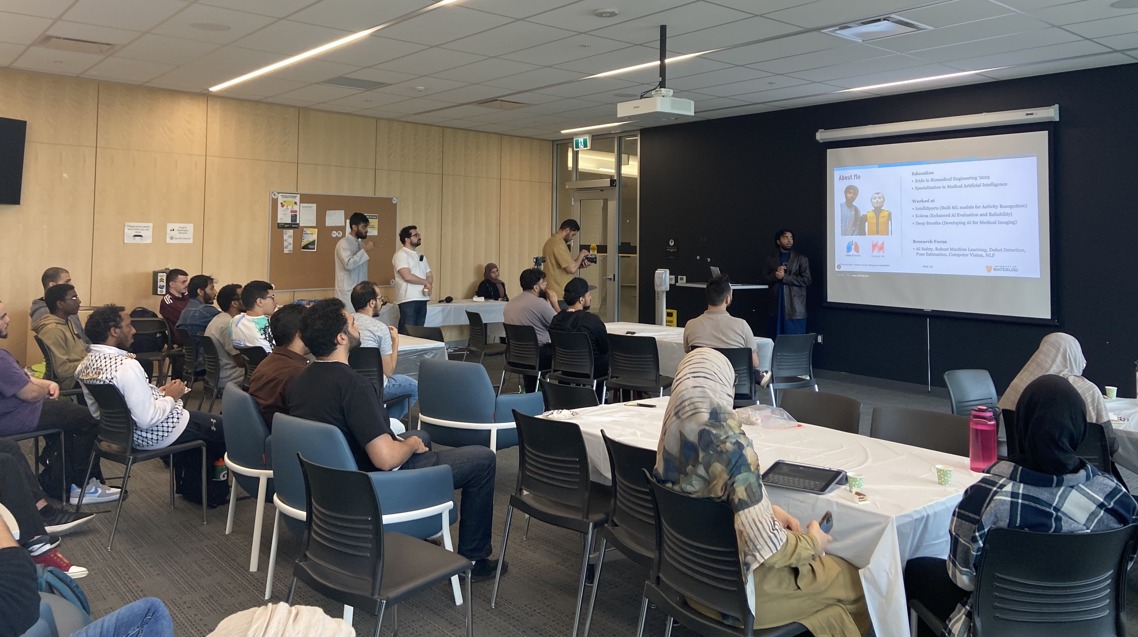 Students sit at tables listening to a person speaking at a research seminar